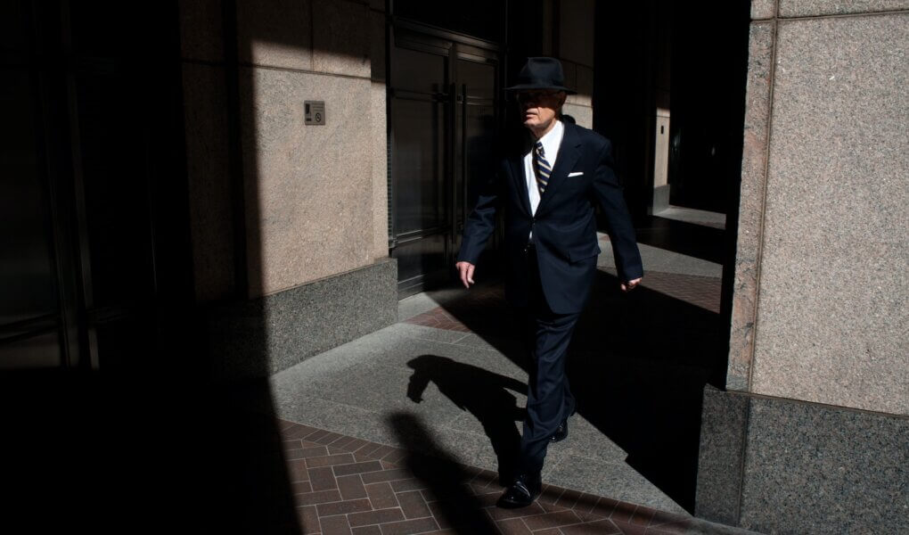 man wearing suit walking on pathway during daytime