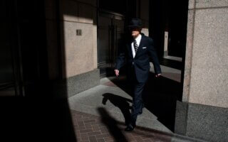 man wearing suit walking on pathway during daytime