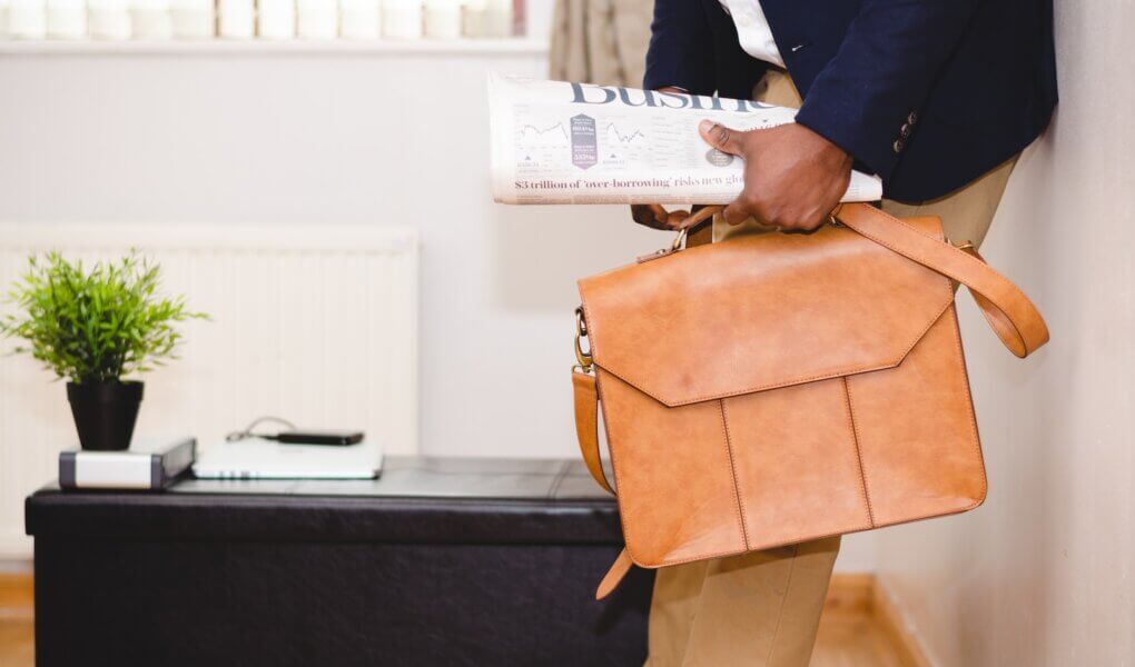 man holding brown leather bag leaning on white wall