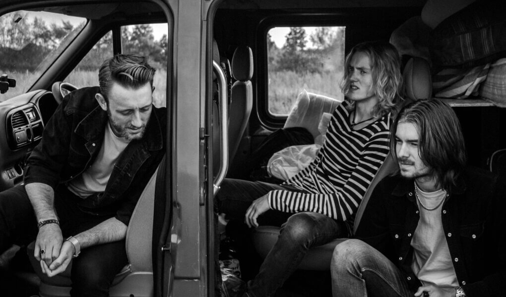 grayscale photo of three men sitting on vehicle seats