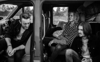 grayscale photo of three men sitting on vehicle seats