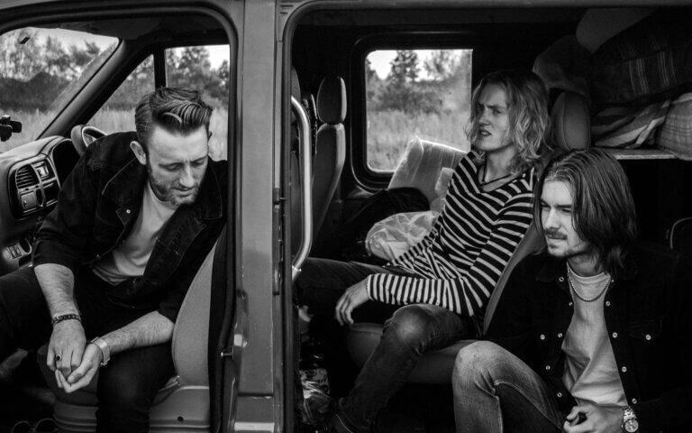 grayscale photo of three men sitting on vehicle seats