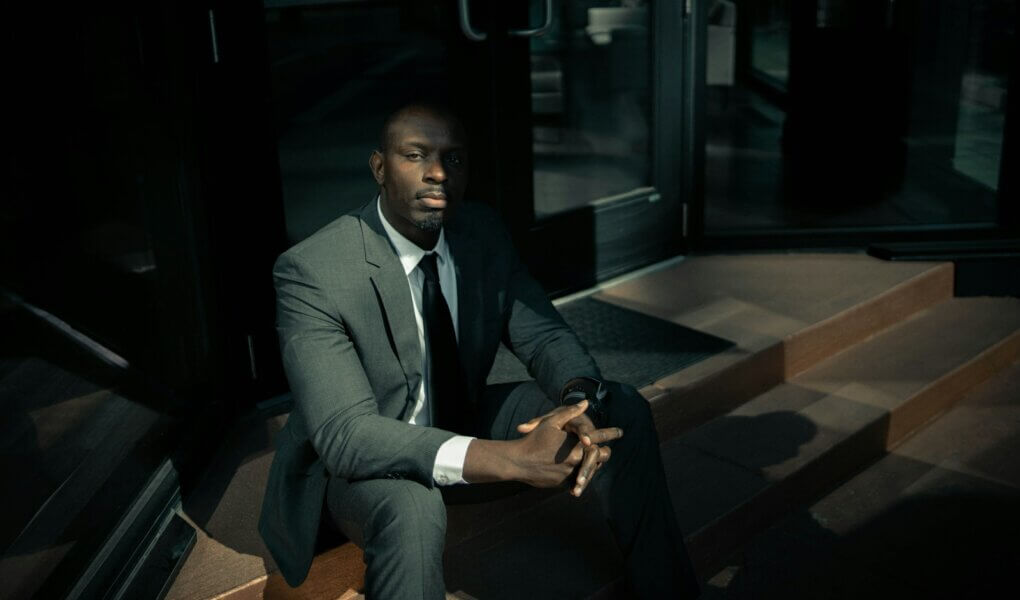 man in black suit sitting on brown wooden bench