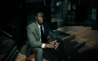 man in black suit sitting on brown wooden bench