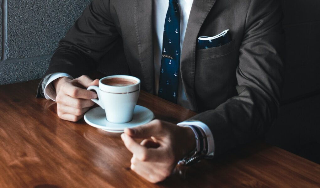 man holding cup filled with coffee on table