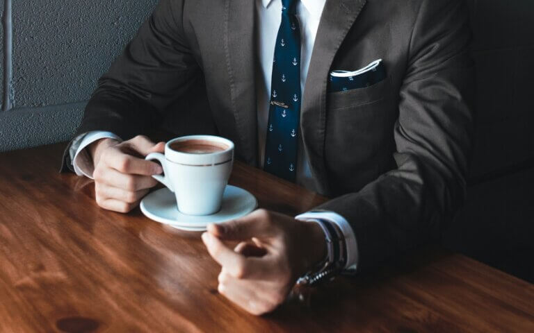 man holding cup filled with coffee on table