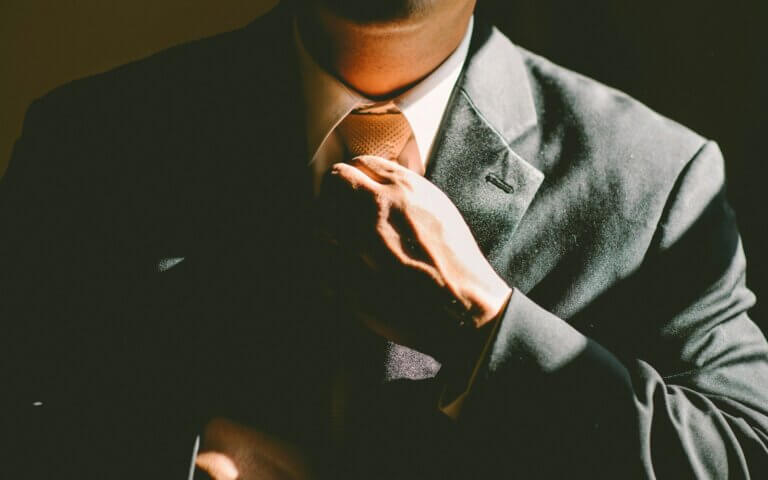 A man in a black suit loosening his tie