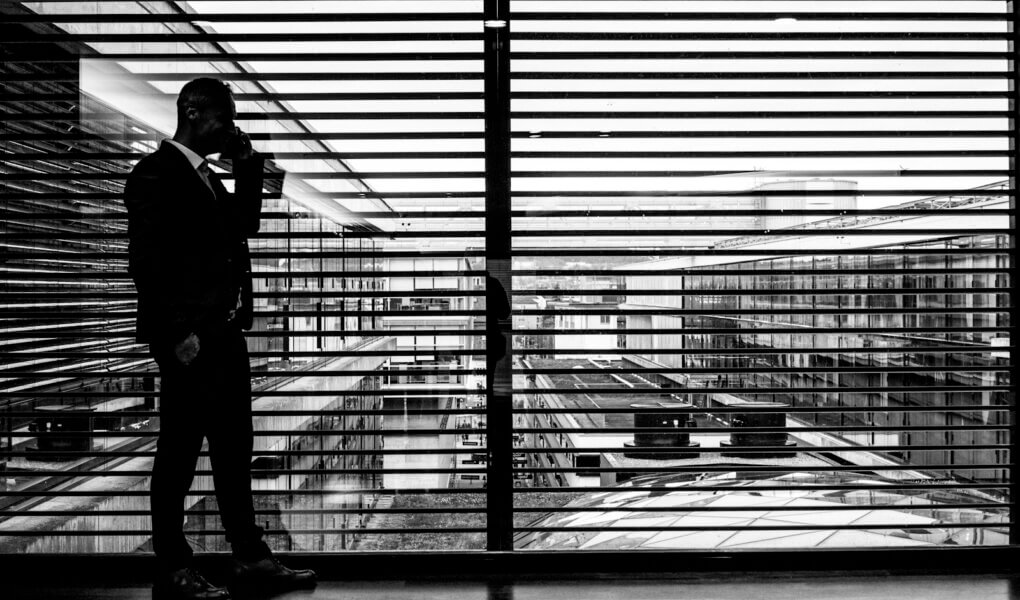 silhouette of man standing beside clear glass wall while using smartphone