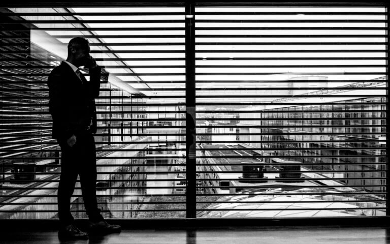 silhouette of man standing beside clear glass wall while using smartphone