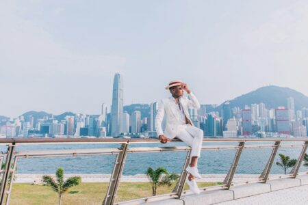 woman in white blazer and white pants sitting on brown wooden railings near body of water