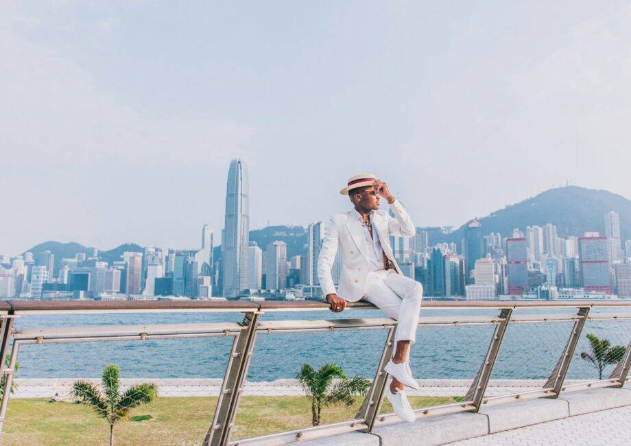 woman in white blazer and white pants sitting on brown wooden railings near body of water