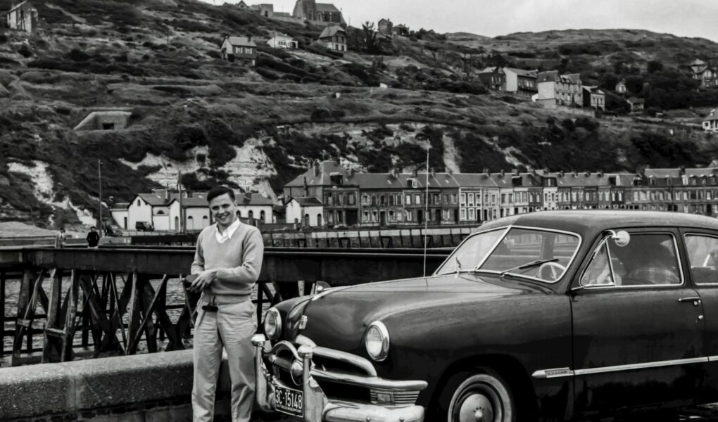 grayscale photography of man standing front of vehicle