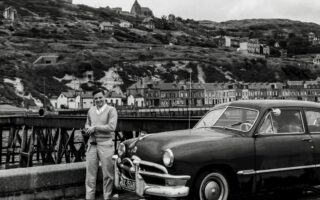 grayscale photography of man standing front of vehicle