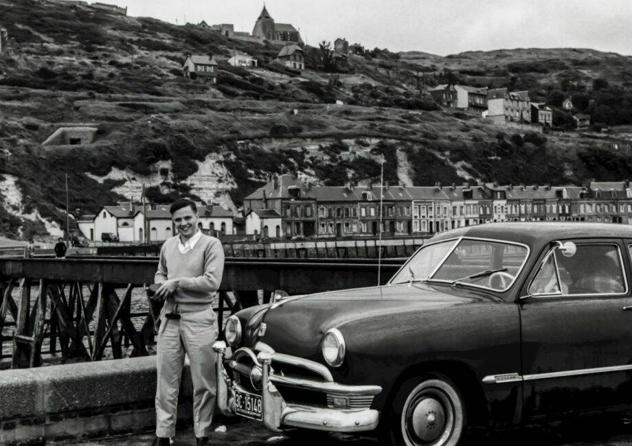 grayscale photography of man standing front of vehicle